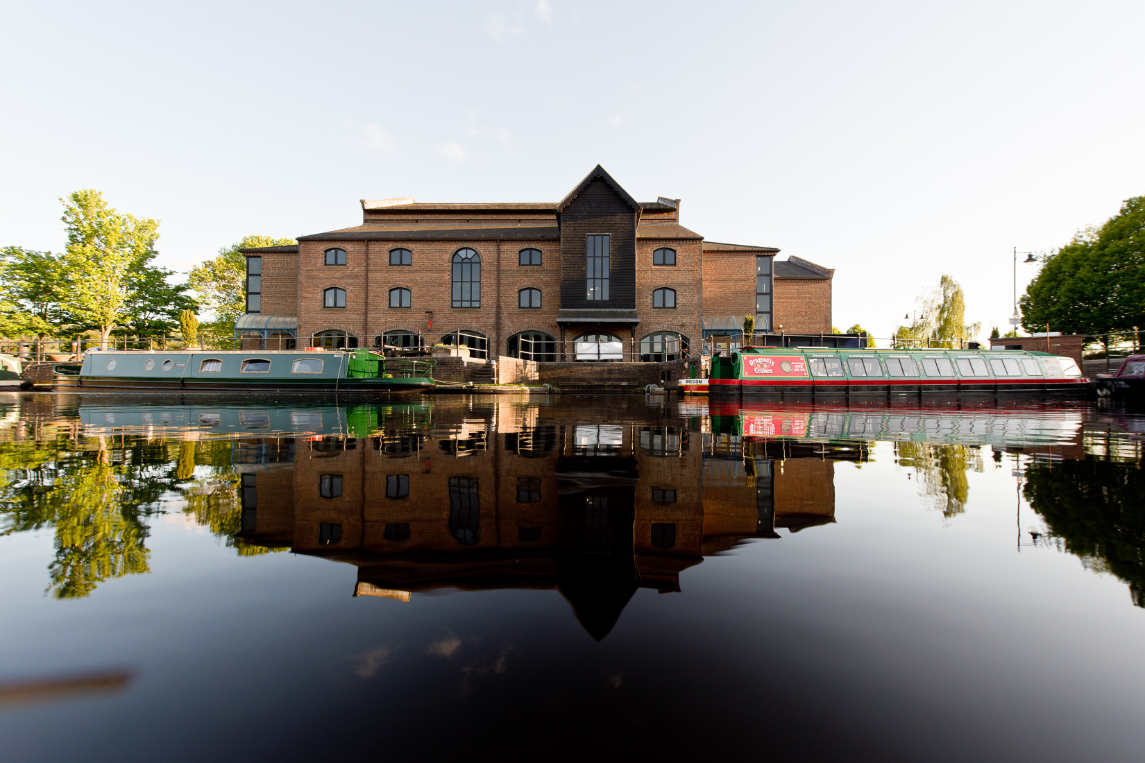 Image of a peaceful looking modern theatre building with its reflection in a body of water