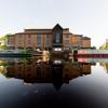 Image of a peaceful looking modern theatre building with its reflection in a body of water